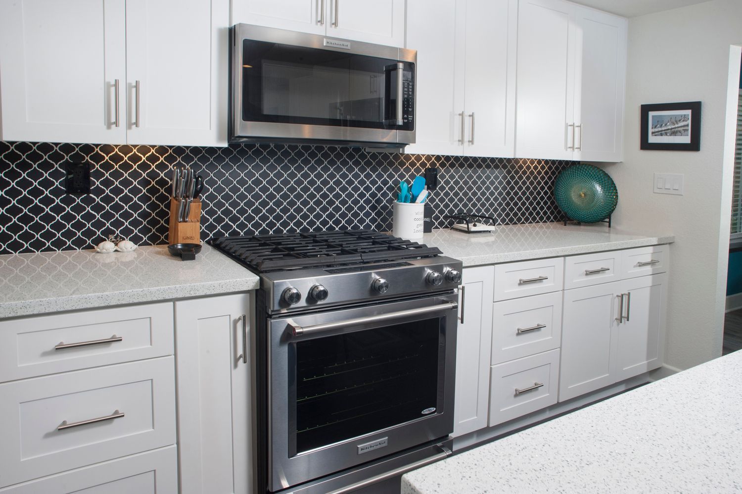 White kitchen with stainless steel appliances, black backsplash, and light countertops.
