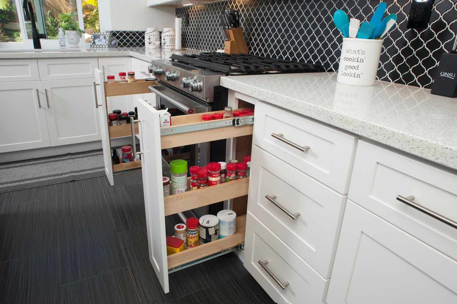 White kitchen with pull-out spice rack beside the stove. Cabinets and countertops are white.