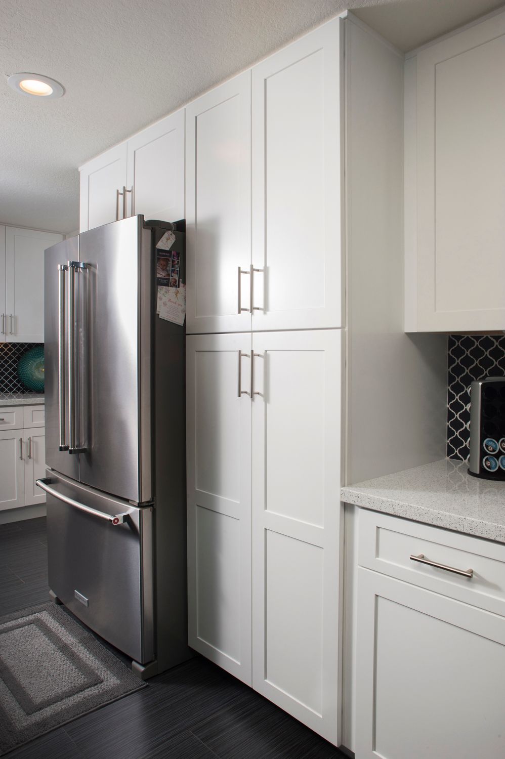 Stainless steel refrigerator beside white cabinets in a kitchen.