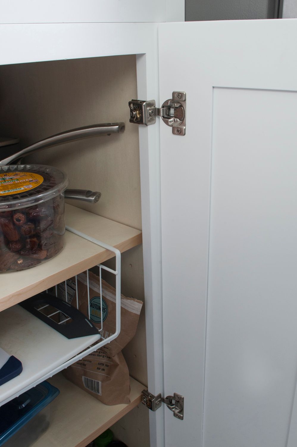White cabinet door open, revealing shelves with a pot, wire basket, and containers.