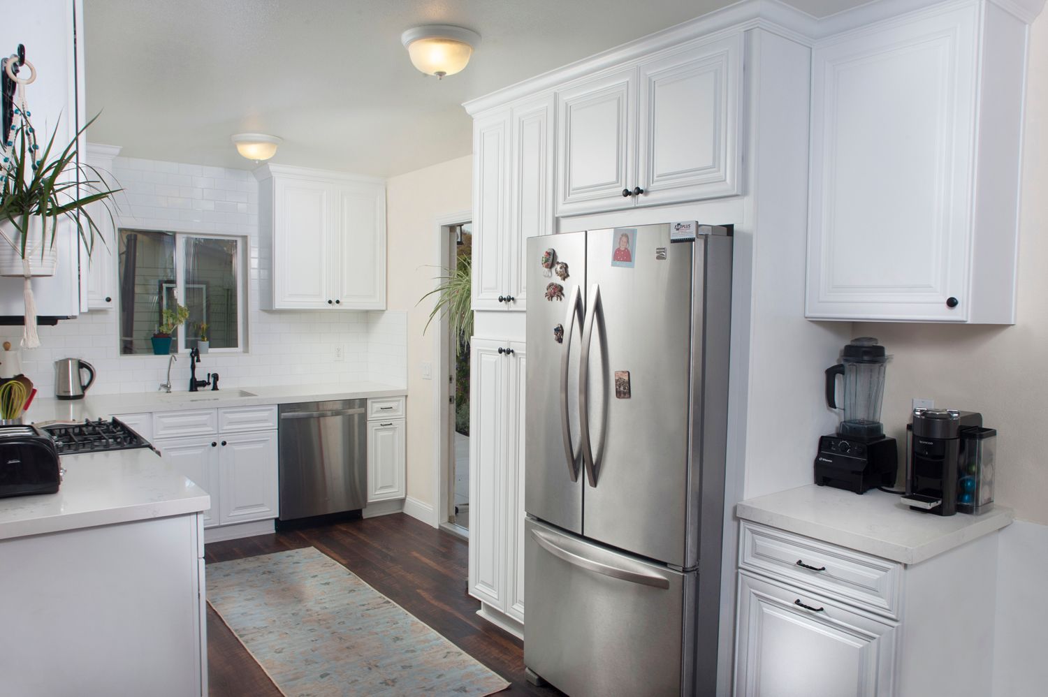 White kitchen with stainless steel appliances, including a refrigerator and dishwasher. Dark wood floors.
