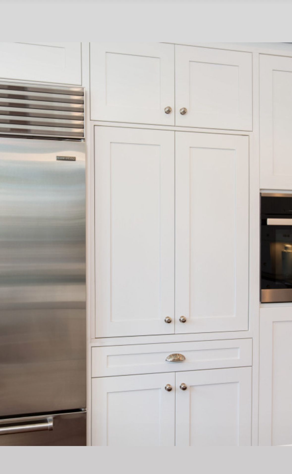 White kitchen cabinets with stainless steel refrigerator and built-in oven.