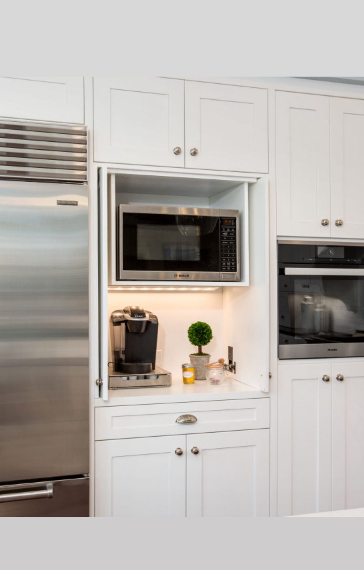 White kitchen cabinet with a microwave, coffee maker, and built-in oven.