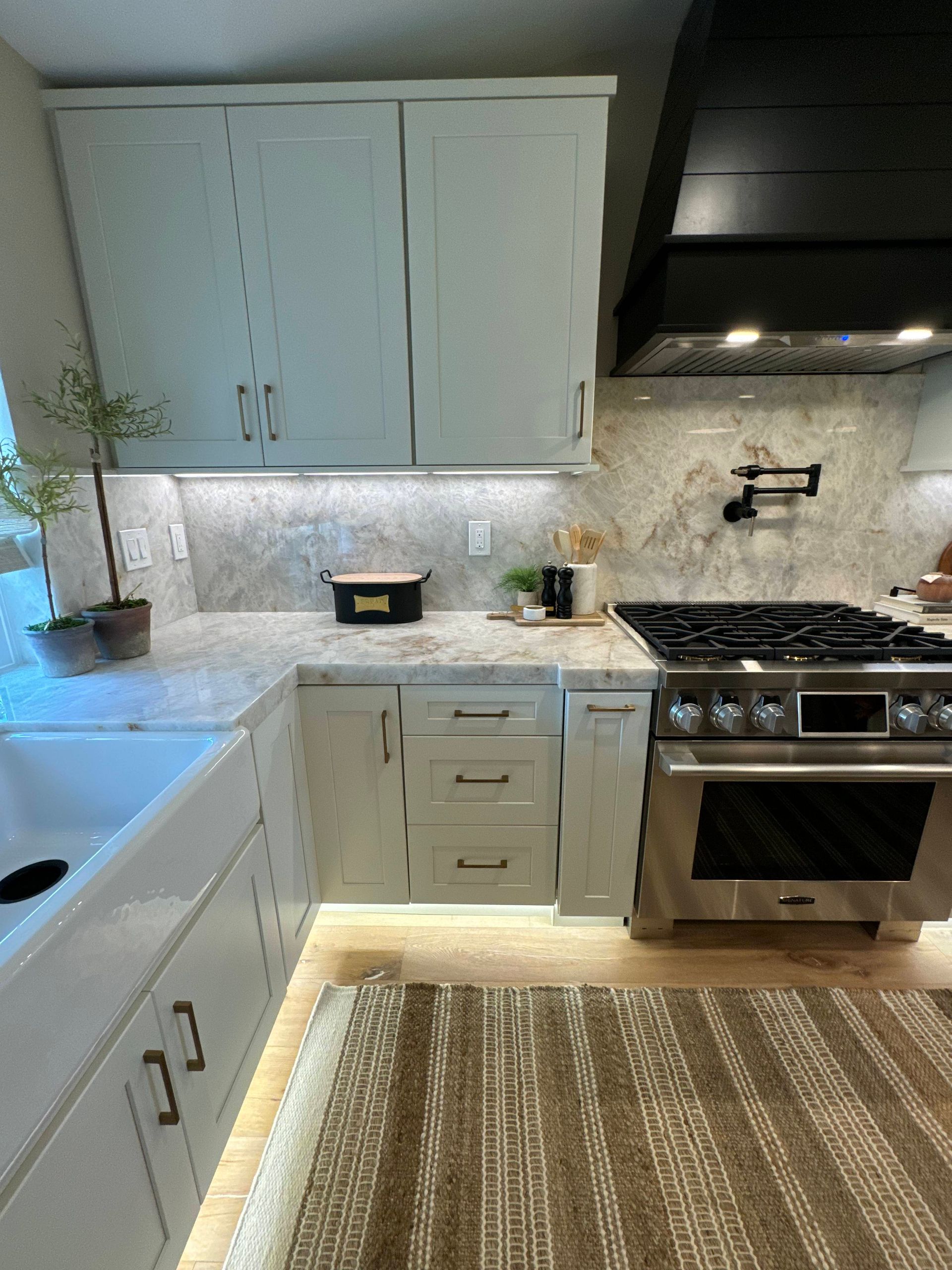 Light gray kitchen with white countertops, stainless steel stove, and overhead cabinets.