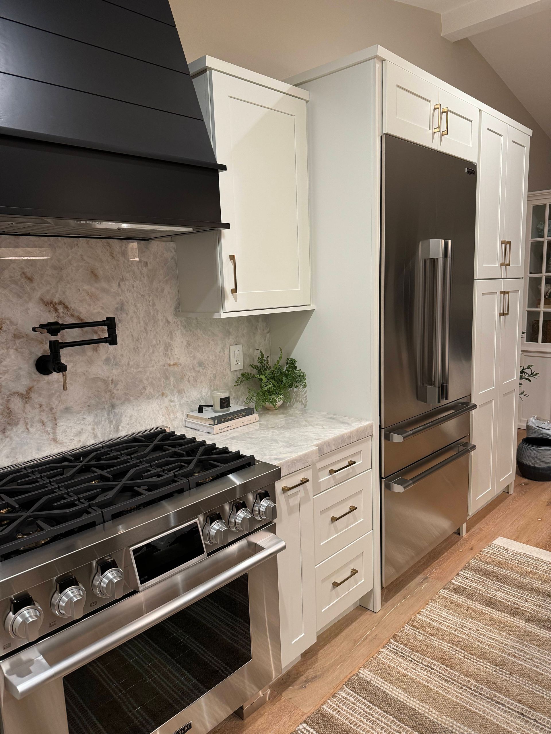 Kitchen with stainless steel refrigerator, white cabinets, marble backsplash, and a black stove.