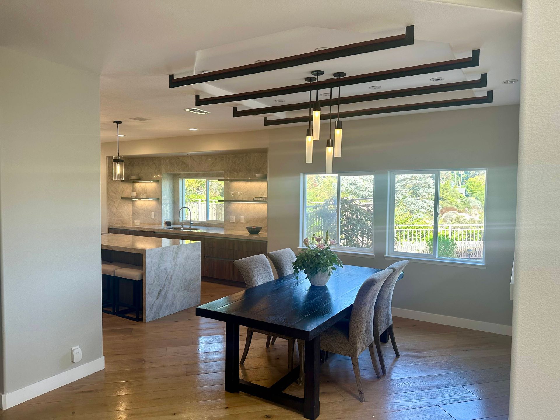 Dining room with dark table and chairs, kitchen in background. Wooden beams on ceiling.