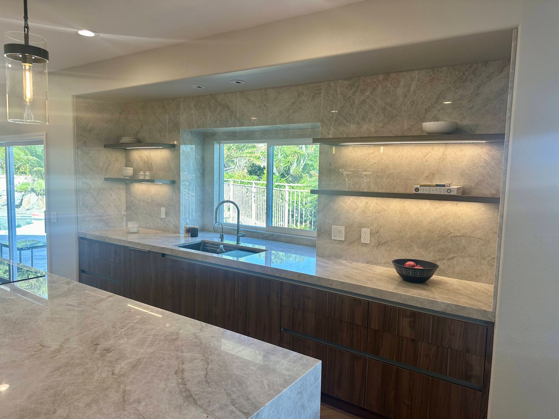 Modern kitchen with stone countertop, wooden cabinets, and recessed shelving with ambient lighting.