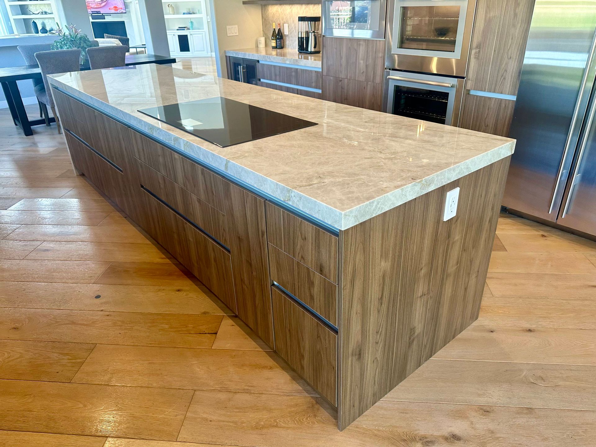 Kitchen island with a light countertop and wood-grain cabinets, and a cooktop.