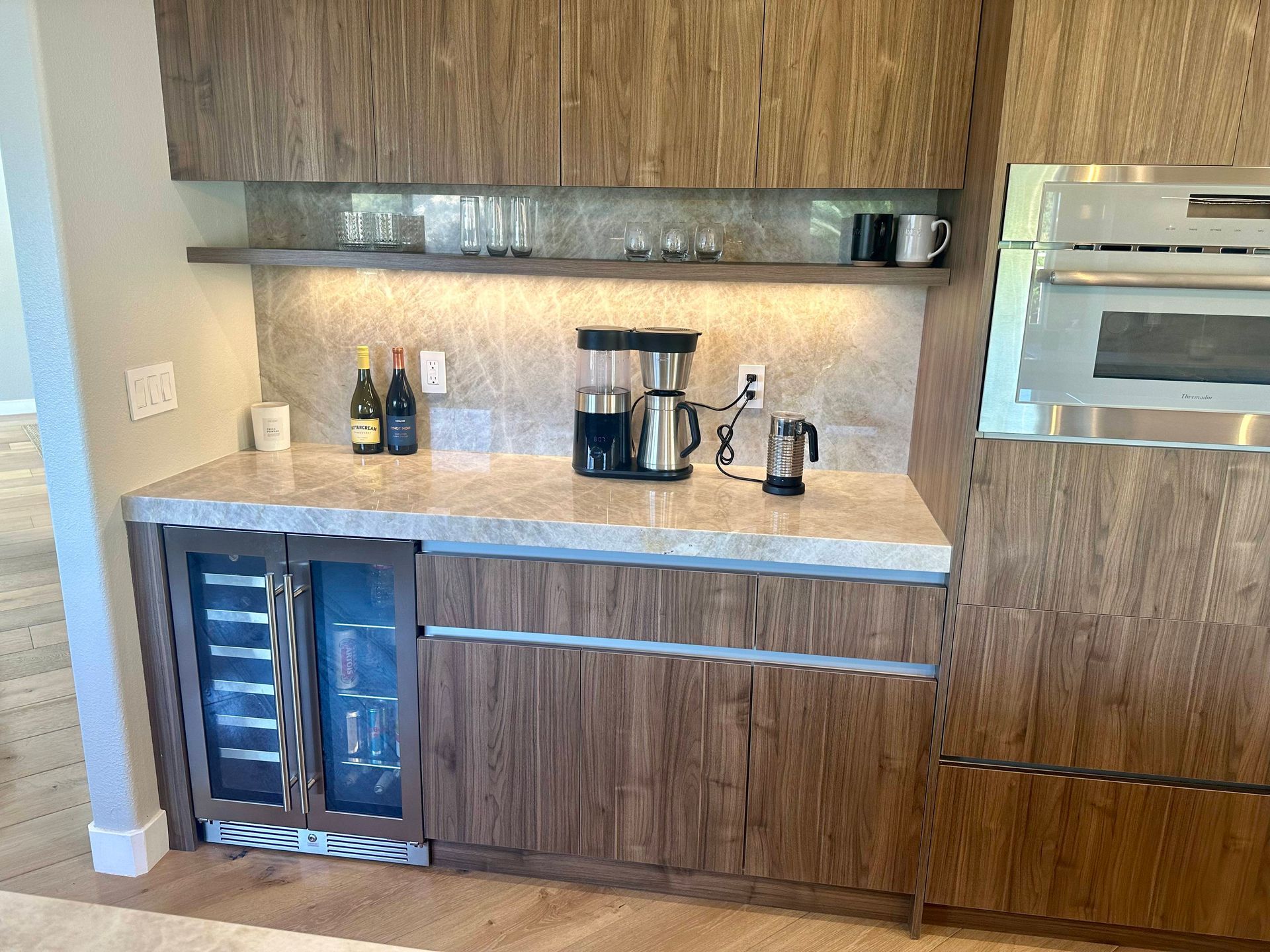 Built-in coffee station with wine fridge, cabinets, countertop, and a microwave in a wood-paneled wall.