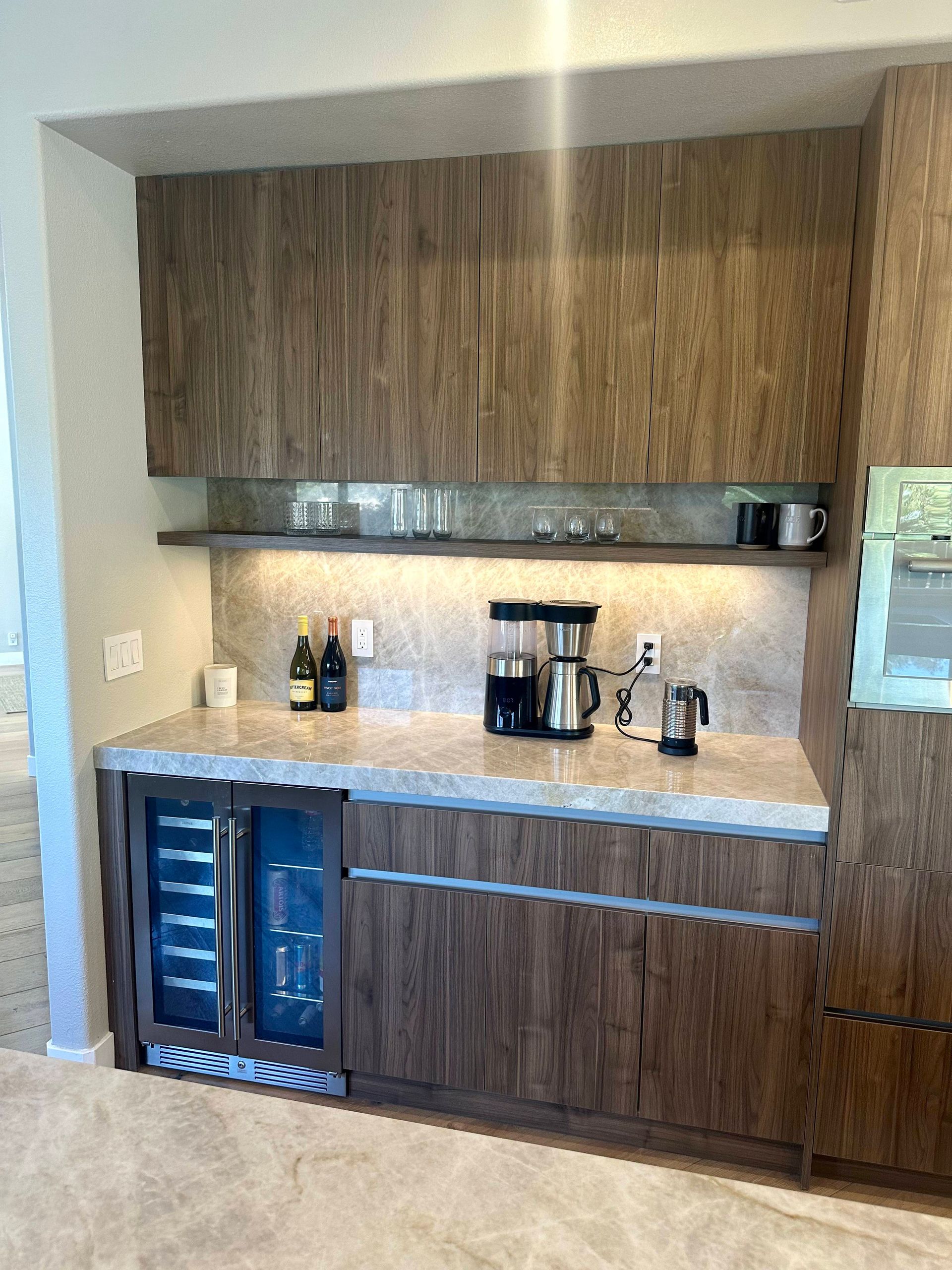 Built-in home bar with wood grain cabinets, wine fridge, coffee maker, and stone countertop.
