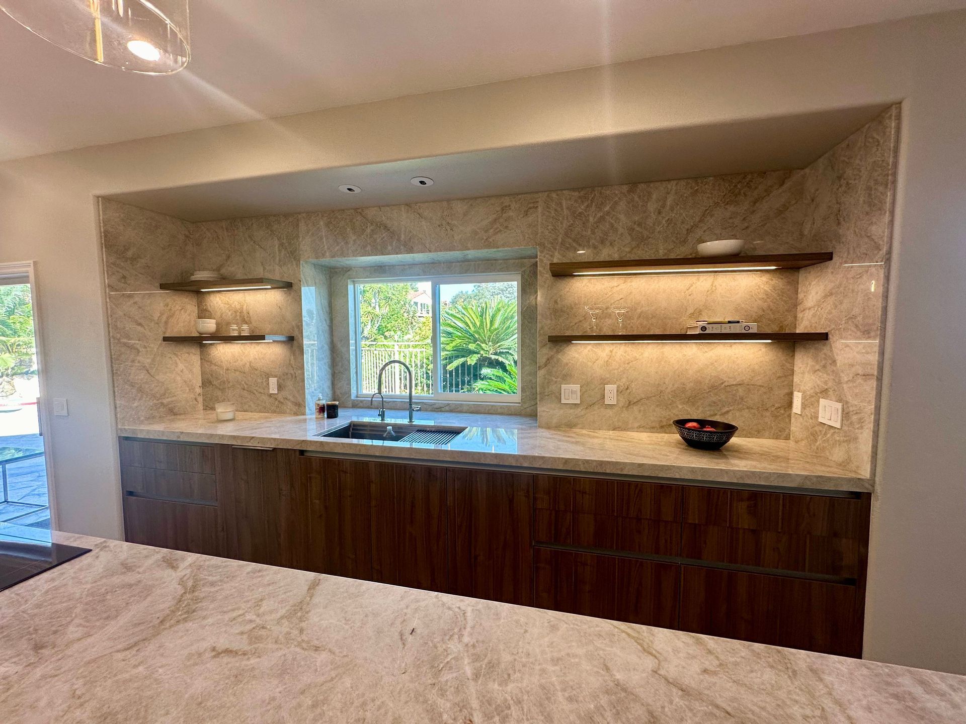 Modern kitchen with marble countertops, dark wood cabinets, and built-in shelves with under-cabinet lighting.