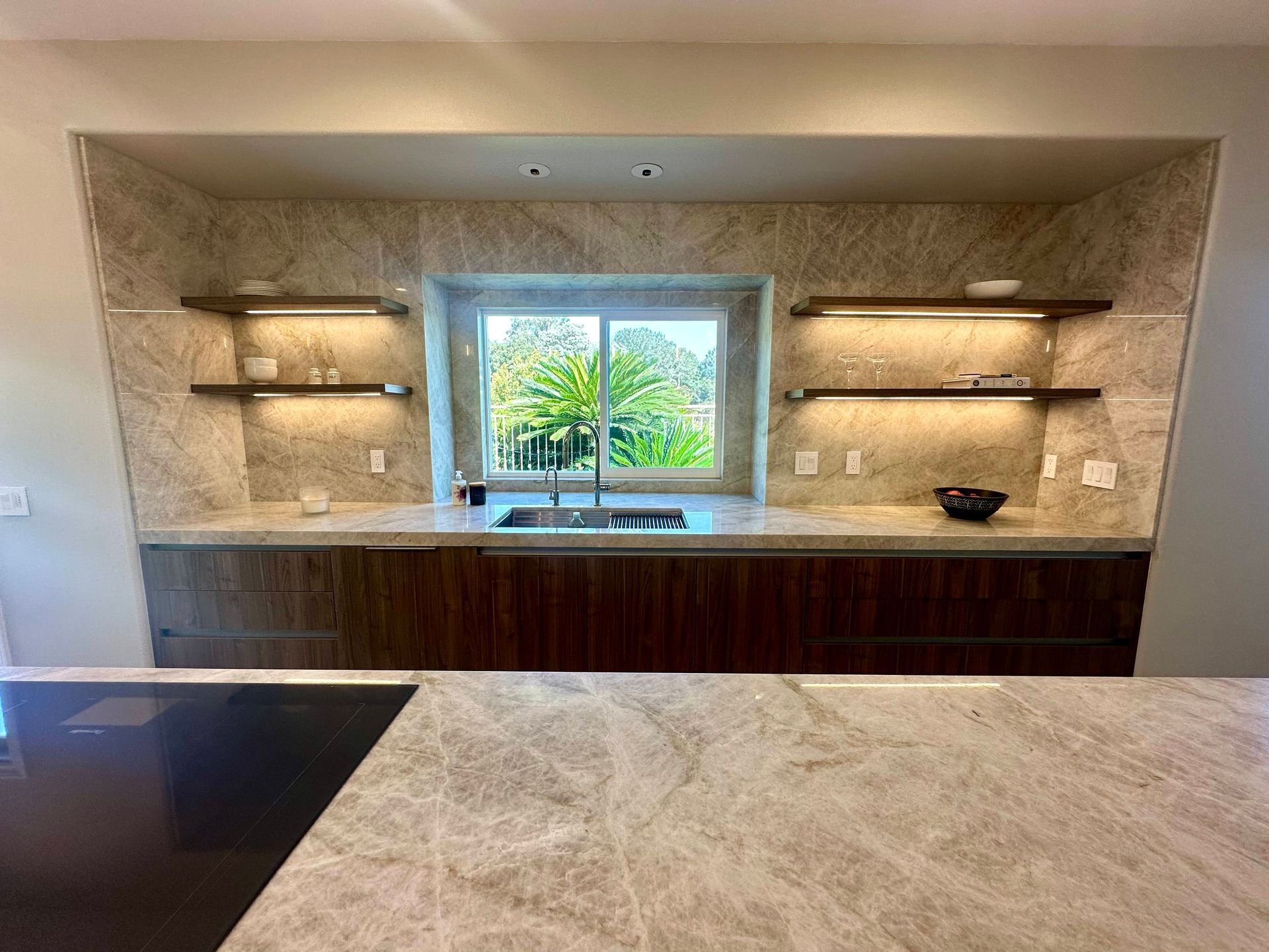 Modern kitchen with a window over a sink, wood cabinets, marble backsplash and shelves.