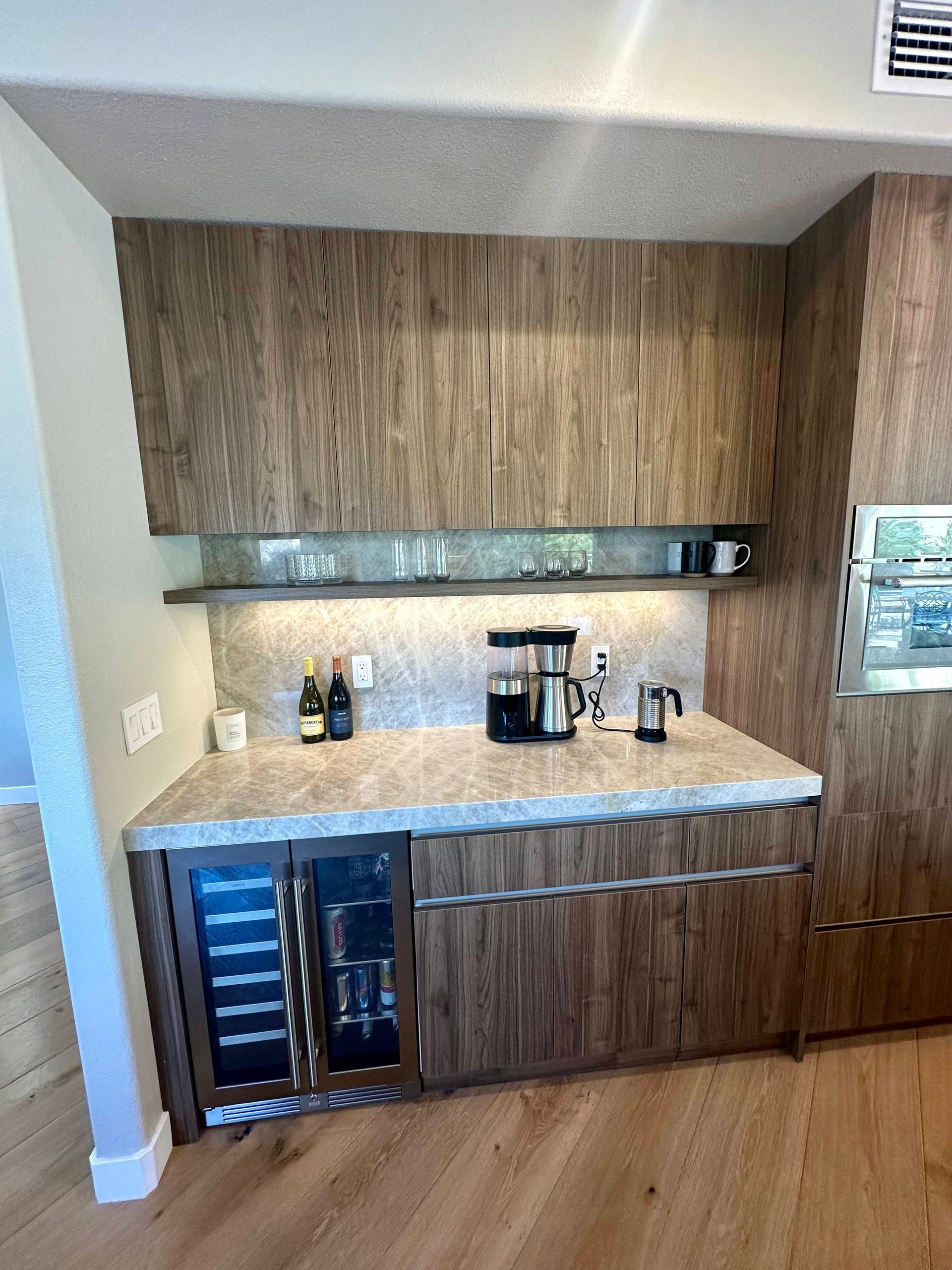 Built-in coffee/wine bar with wood cabinets, wine fridge, coffee maker, and shelves.