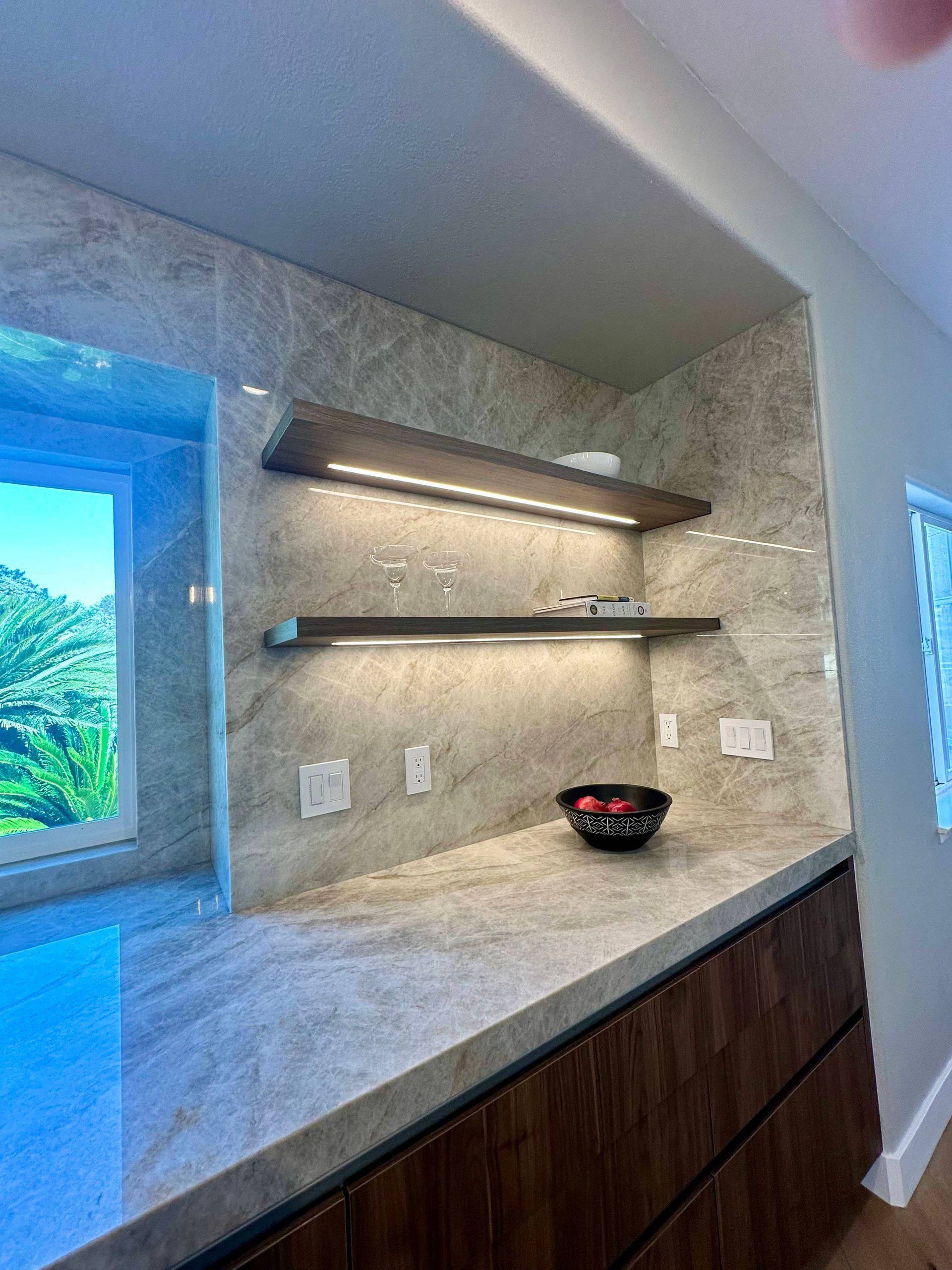 Built-in kitchen counter with marble backsplash, floating shelves, and under-shelf lighting.