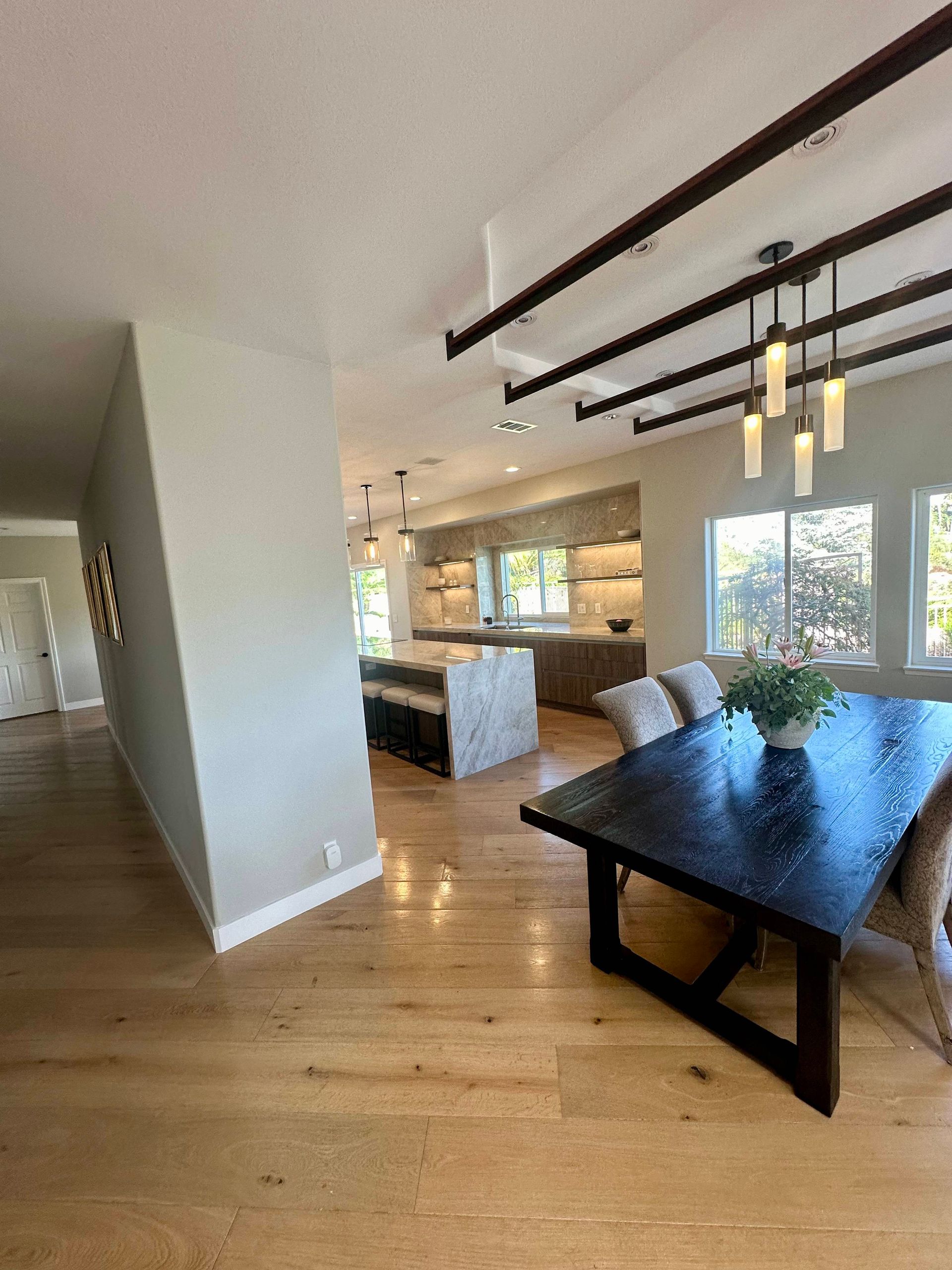 Modern open-concept kitchen and dining area with wood floors, island, and dark wood beams.