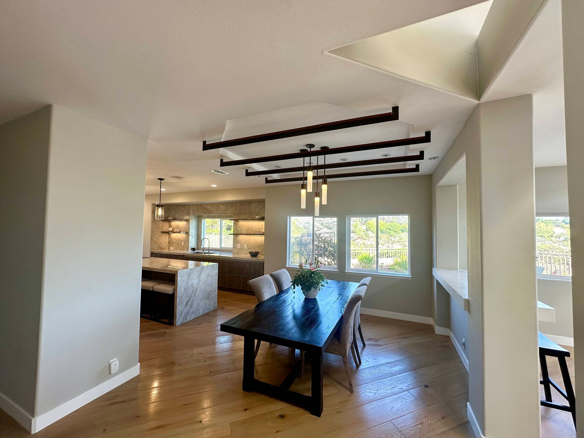 Dining room with black table, chairs, and chandelier; adjacent kitchen with island.