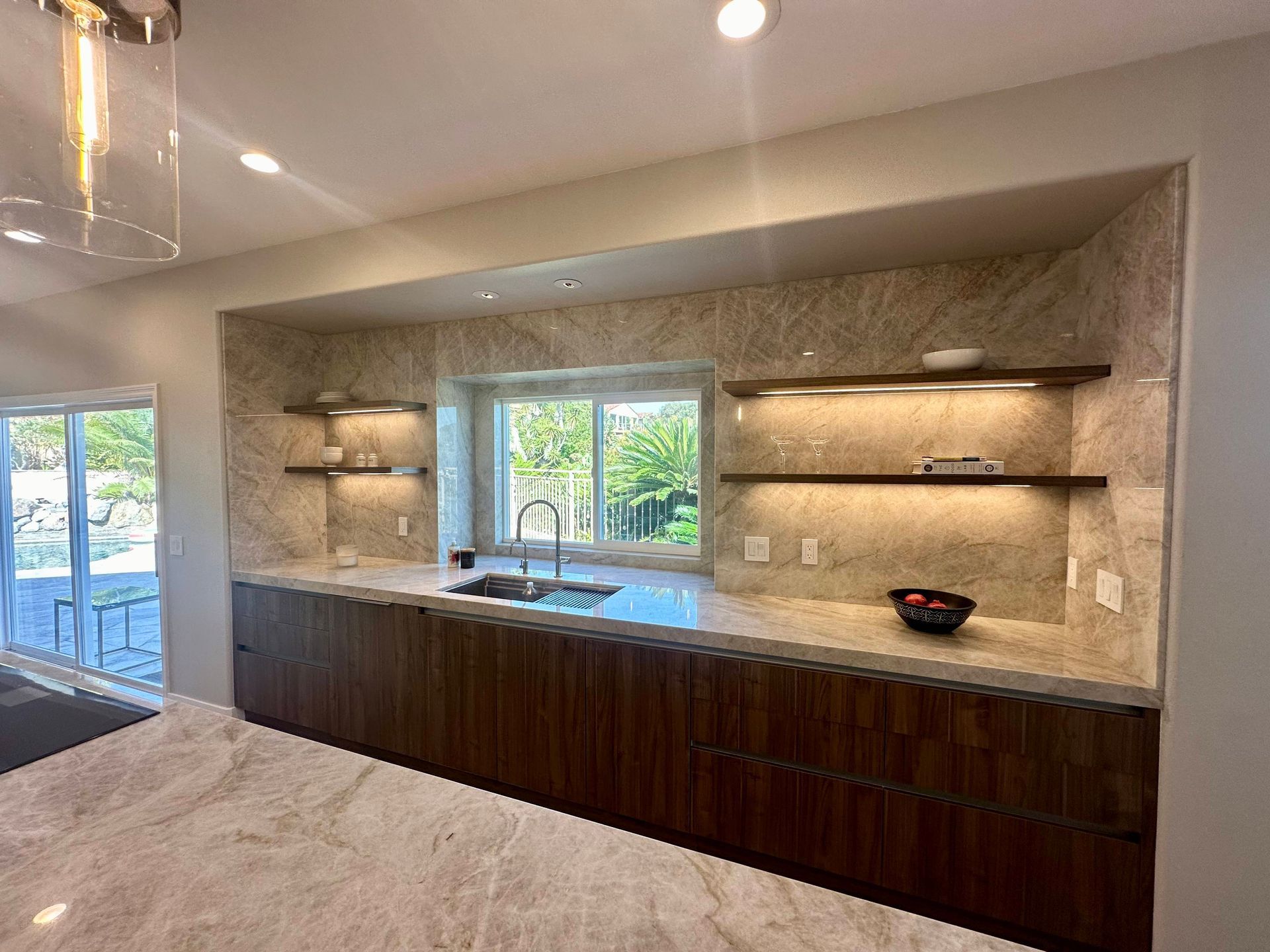 Modern kitchen with built-in cabinetry, marble backsplash, floating shelves, and window above sink.