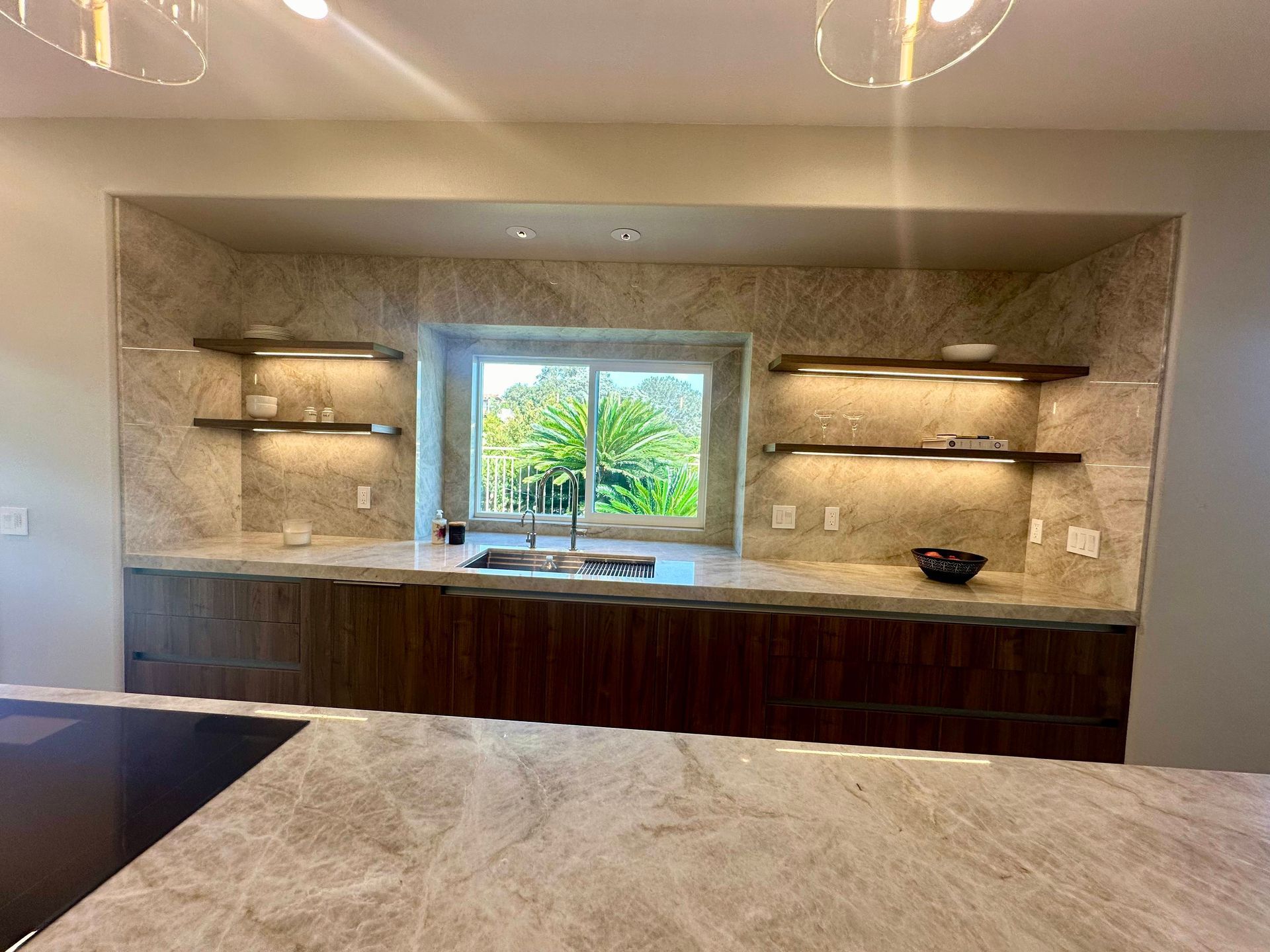 Kitchen with wood cabinets, stone backsplash and countertop, stainless steel sink under a window.