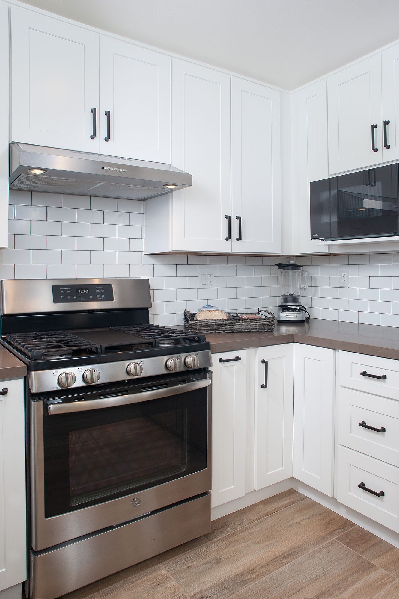 White kitchen with stainless steel appliances, white cabinets, and brown countertop.