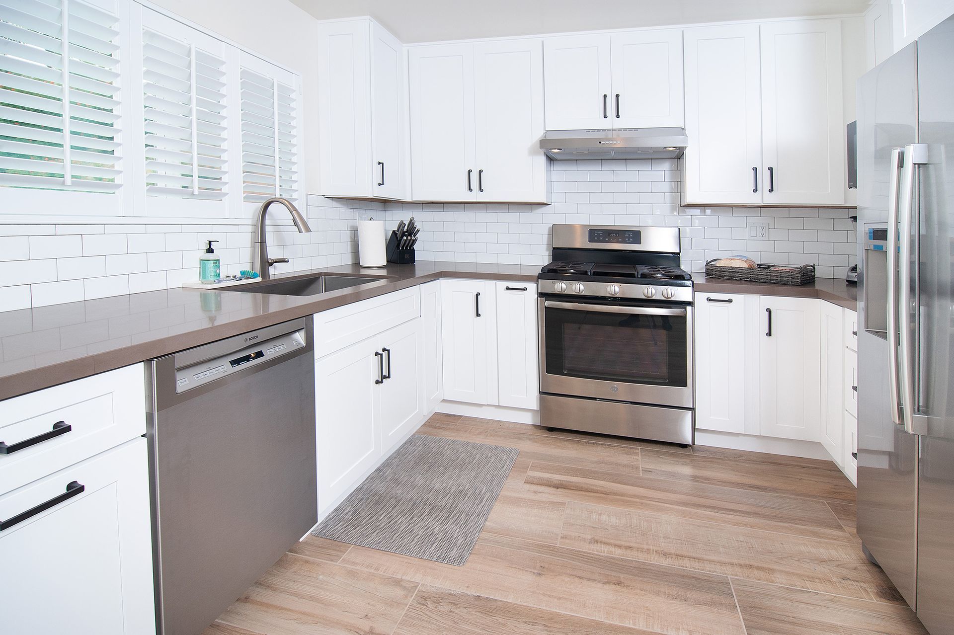 White kitchen with stainless steel appliances, gray countertops, and wood-look flooring.