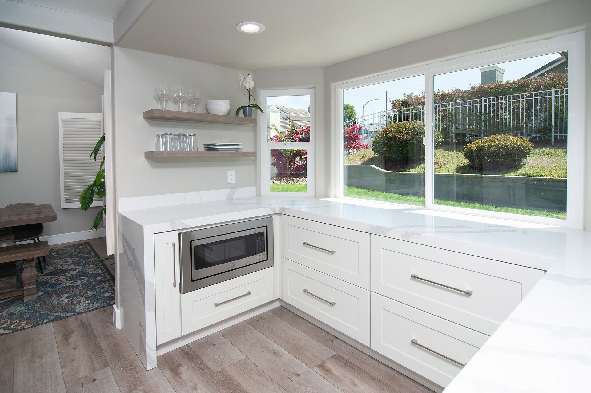 Modern white kitchen with large window, microwave, and light wood floors.