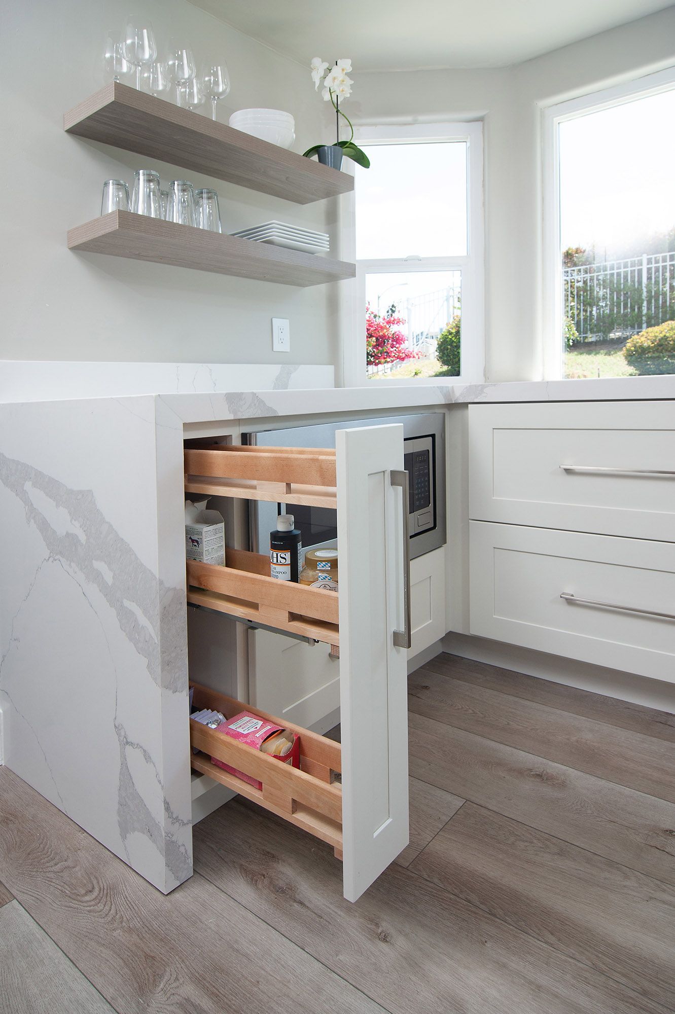 Pull-out pantry cabinet in a white kitchen with wooden shelves, countertop, and a built-in microwave.