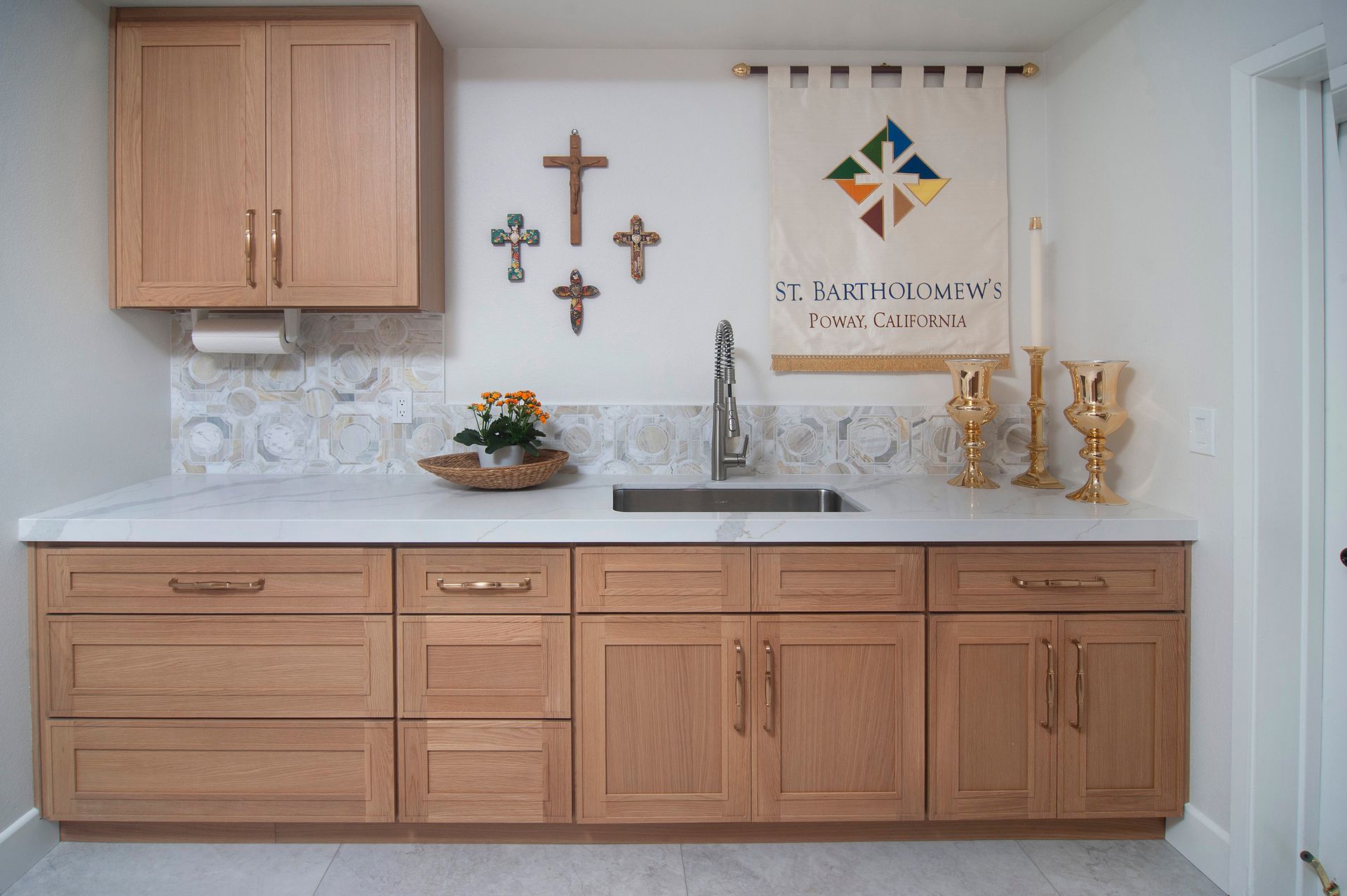 Oak cabinets, sink, crosses, and religious banner in a light-filled, clean space.