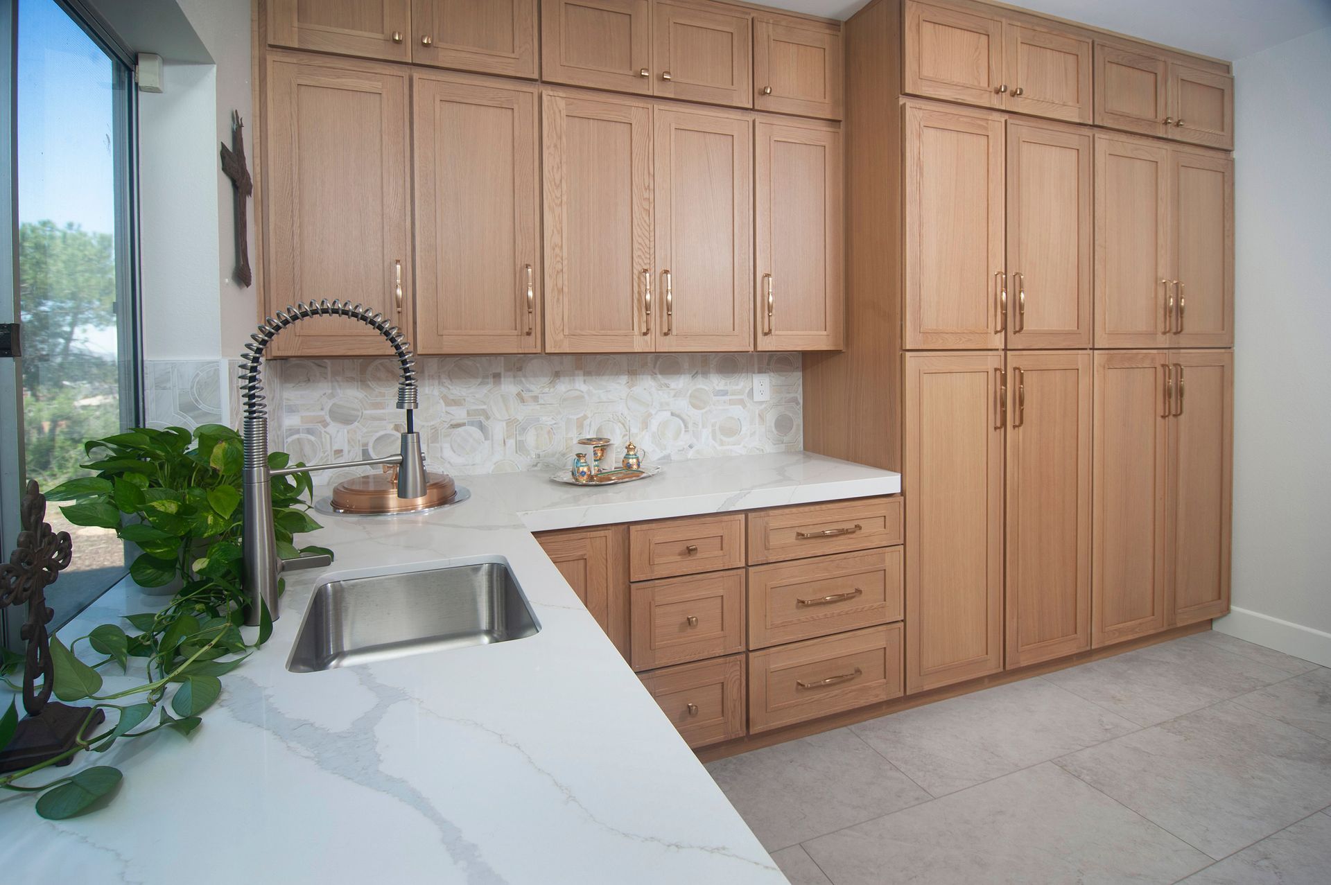 Light wood cabinets and countertops in a kitchen, with a sink and a tall storage unit.