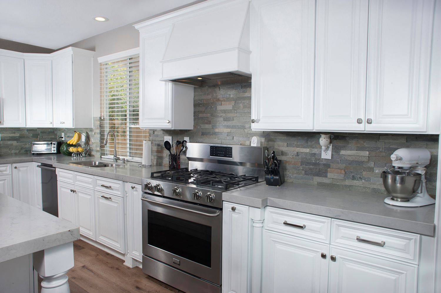 White kitchen with stainless steel appliances, gray countertops, and a stone backsplash.