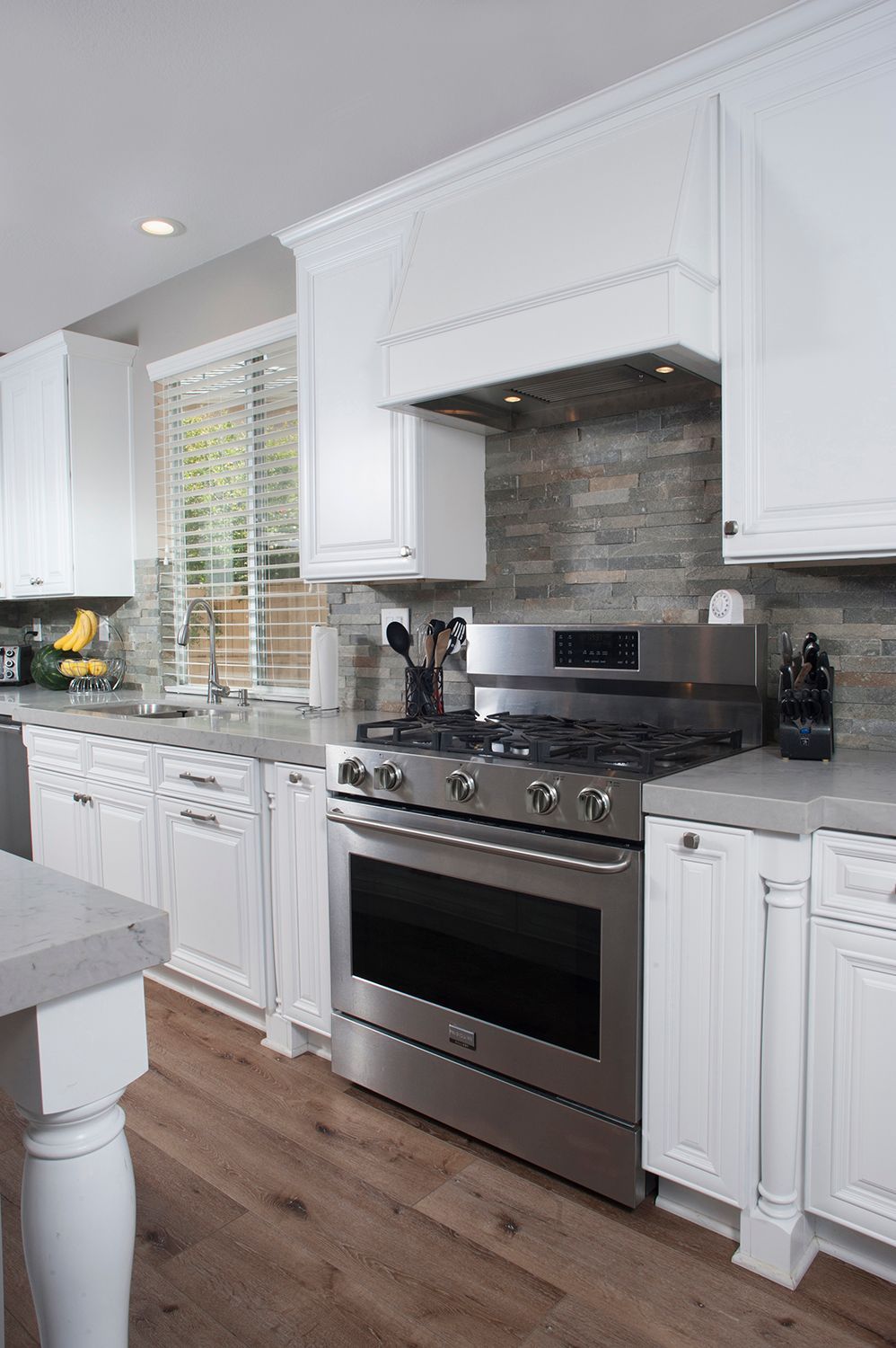 White kitchen with stainless steel range, wooden floor, and gray countertop.
