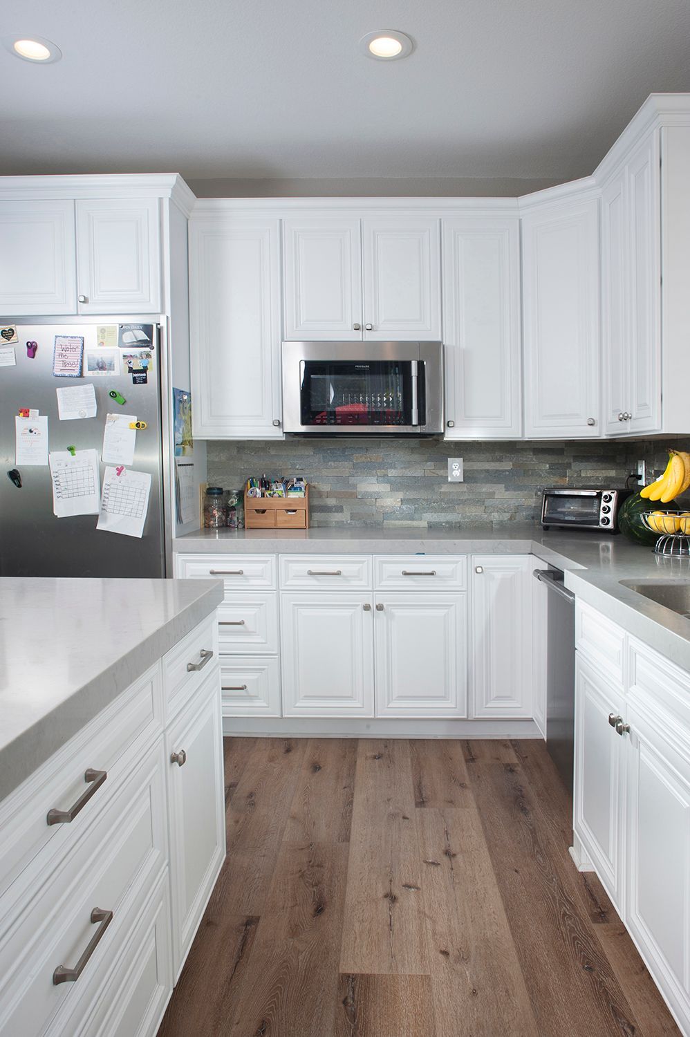 White kitchen with stainless steel appliances, grey countertops, and wood flooring.