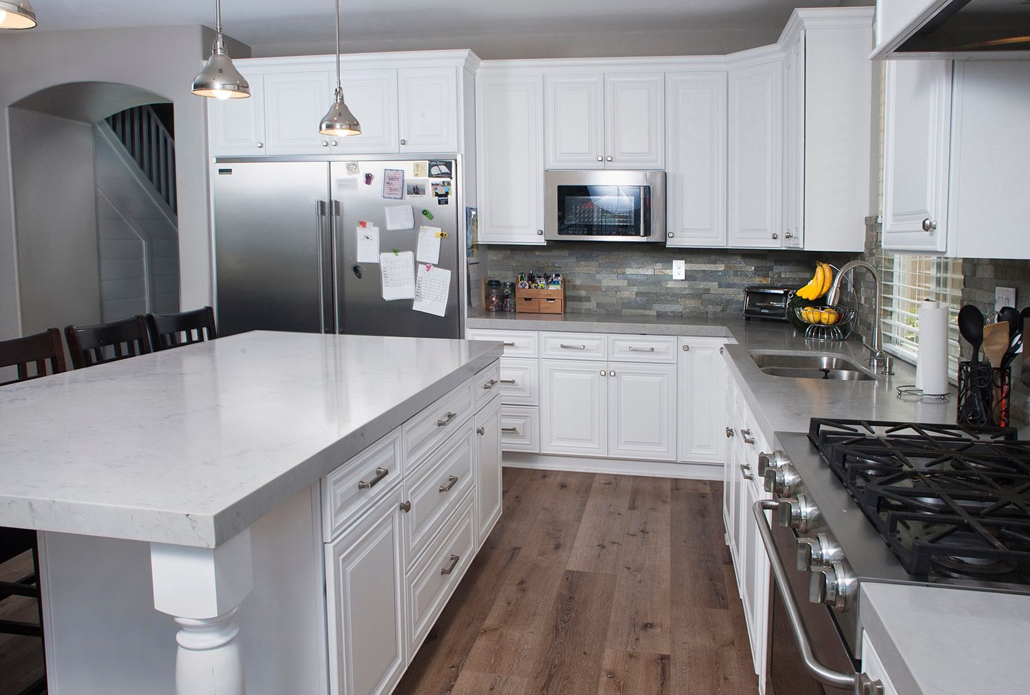 White kitchen with island, stainless steel appliances, and wooden floors.