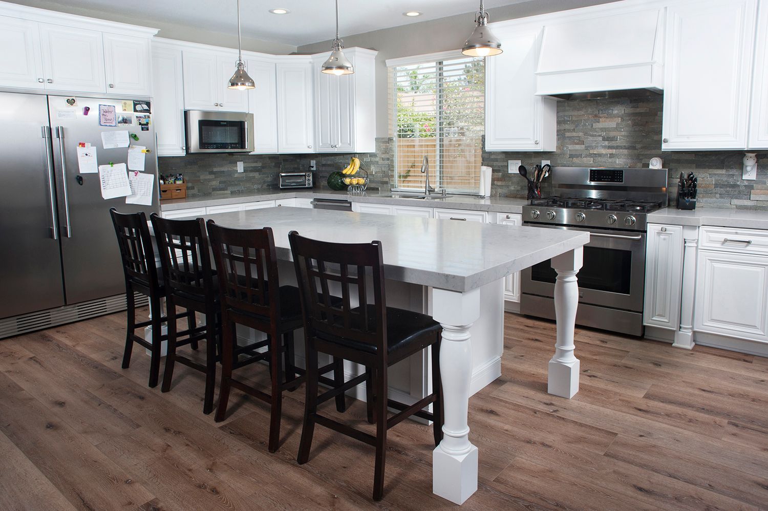 White kitchen with a large island, stainless steel appliances, and dark bar stools.