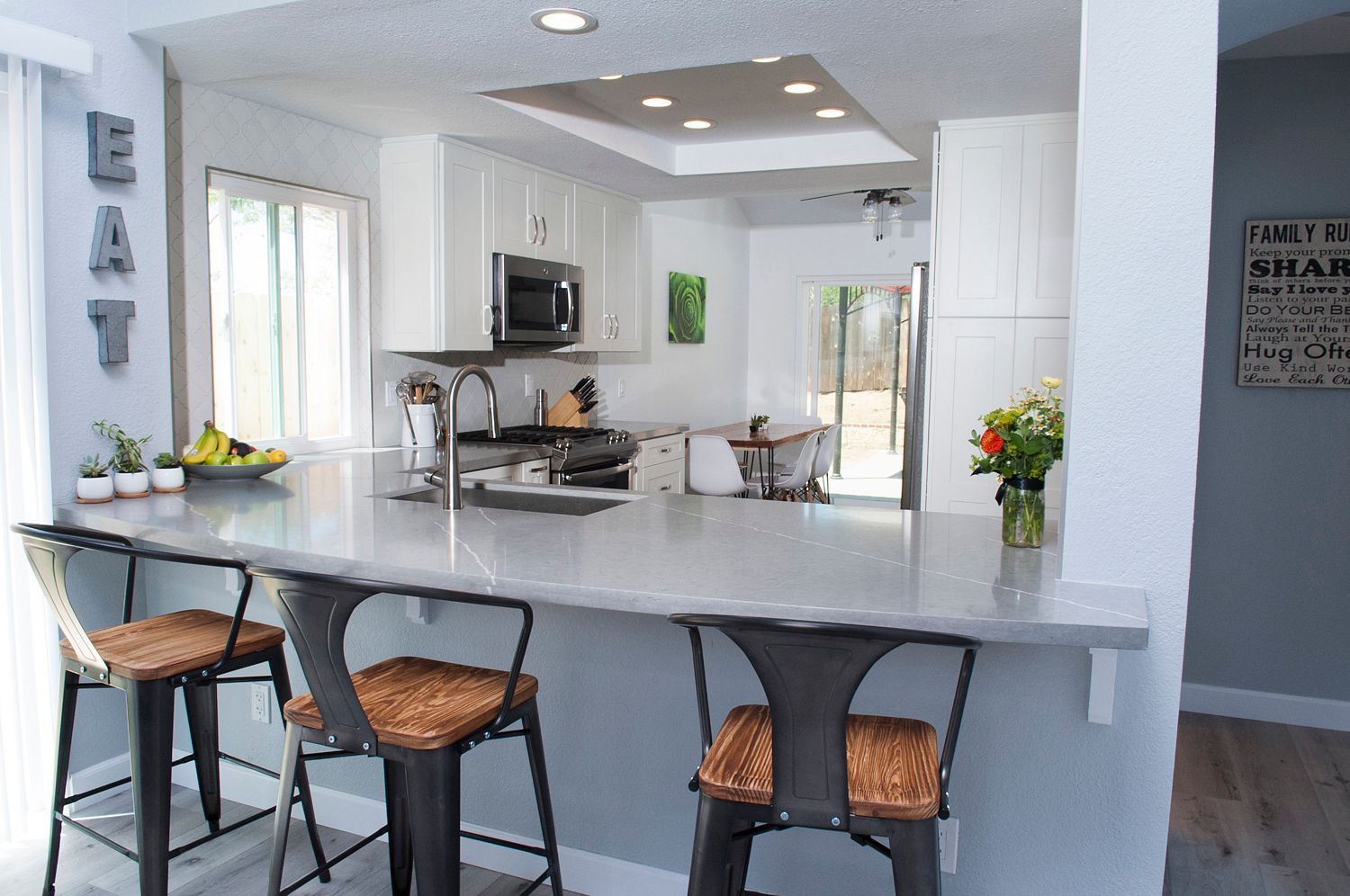Kitchen with a gray island and three bar stools. White cabinets and a skylight are visible.