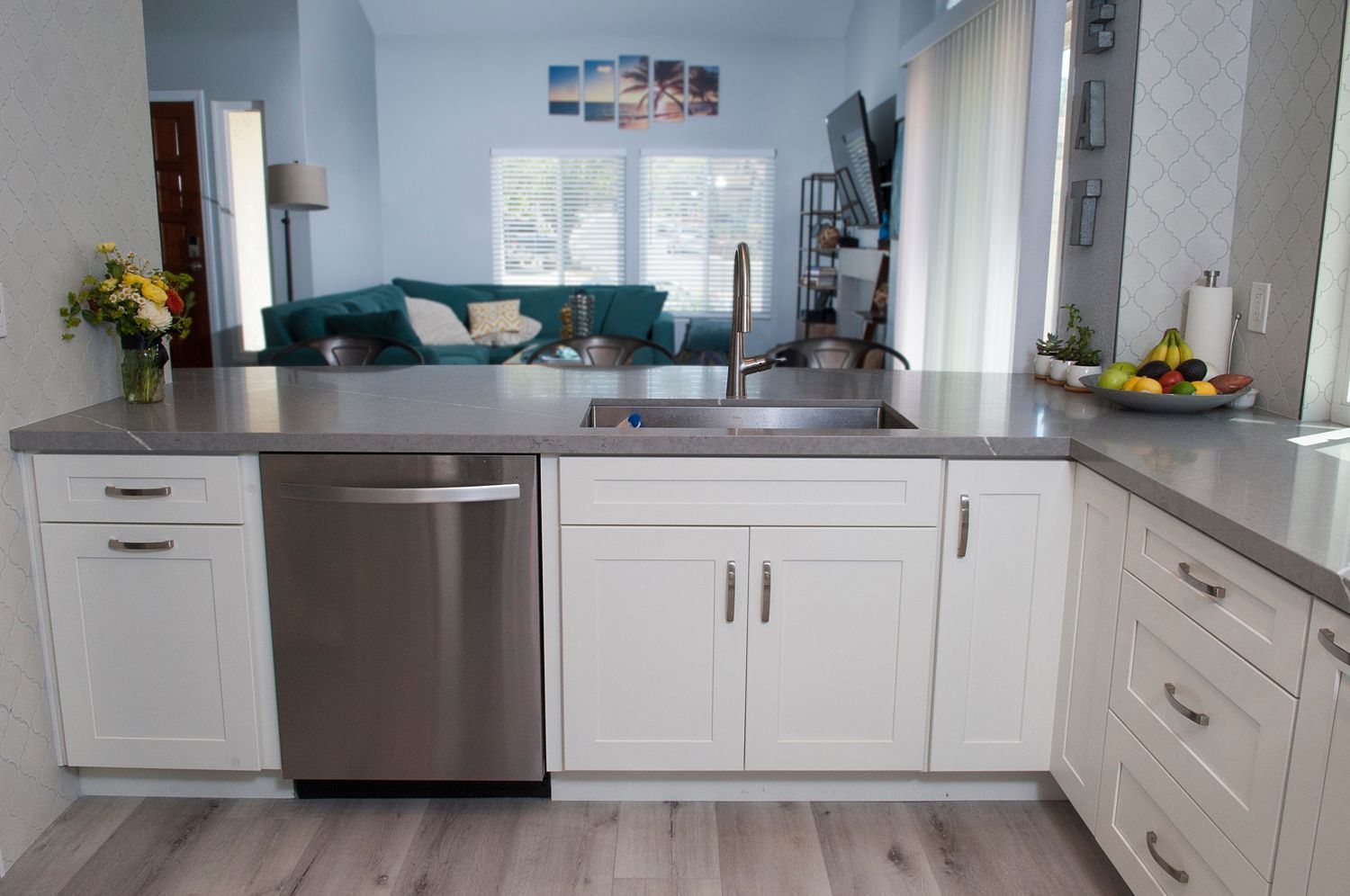 Kitchen with white cabinets, stainless steel dishwasher, grey countertop, and a view into a living room.