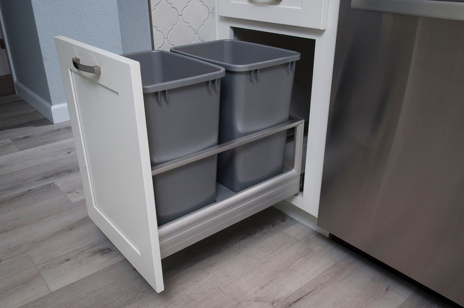 White cabinet pull-out trash and recycling bins. Grey bins on two tiers in kitchen.
