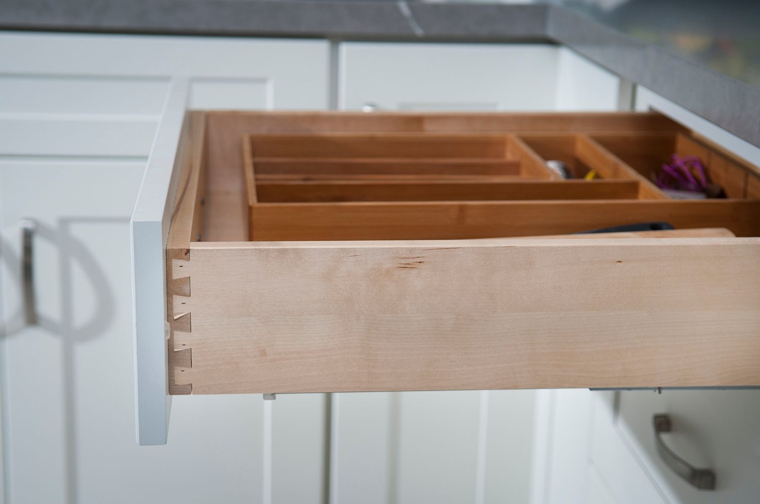Open kitchen drawer, wooden organizer, white cabinetry, gray countertop.