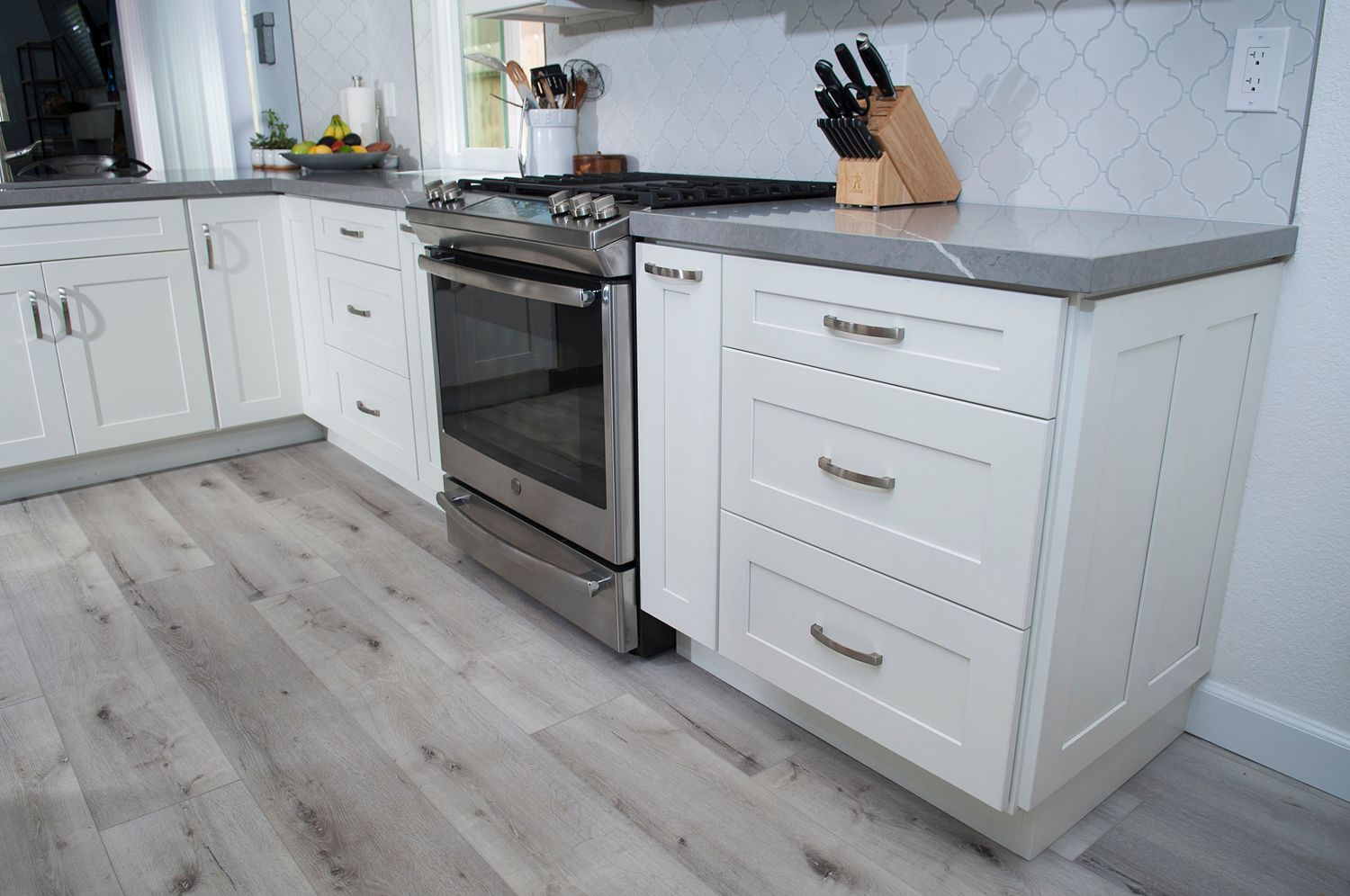White kitchen cabinets with gray countertops. Stainless steel oven and light wood floors.