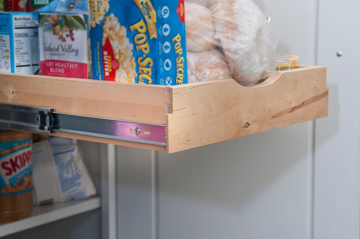 Wooden pull-out pantry shelf with food items like popcorn and bread.