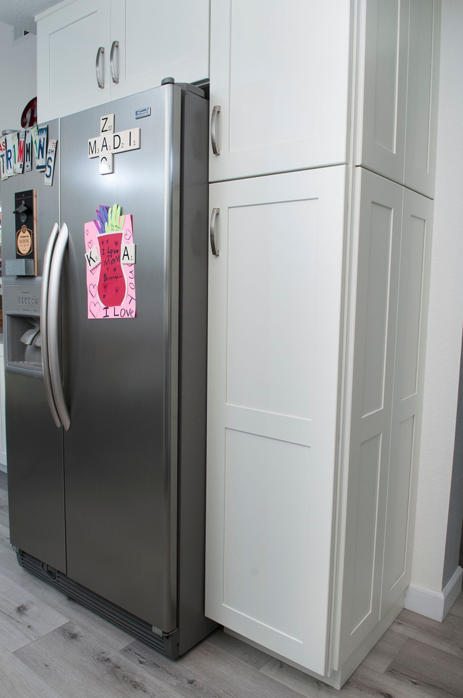 Stainless steel refrigerator next to a tall white pantry cabinet in a kitchen.