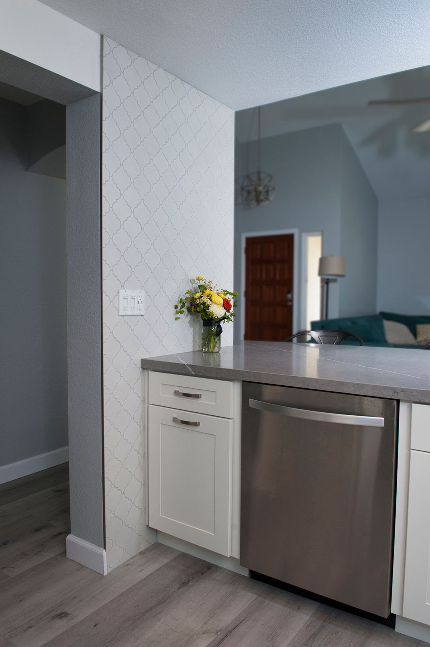 Kitchen with a stainless steel dishwasher, off-white cabinets, gray countertop, and floral arrangement.