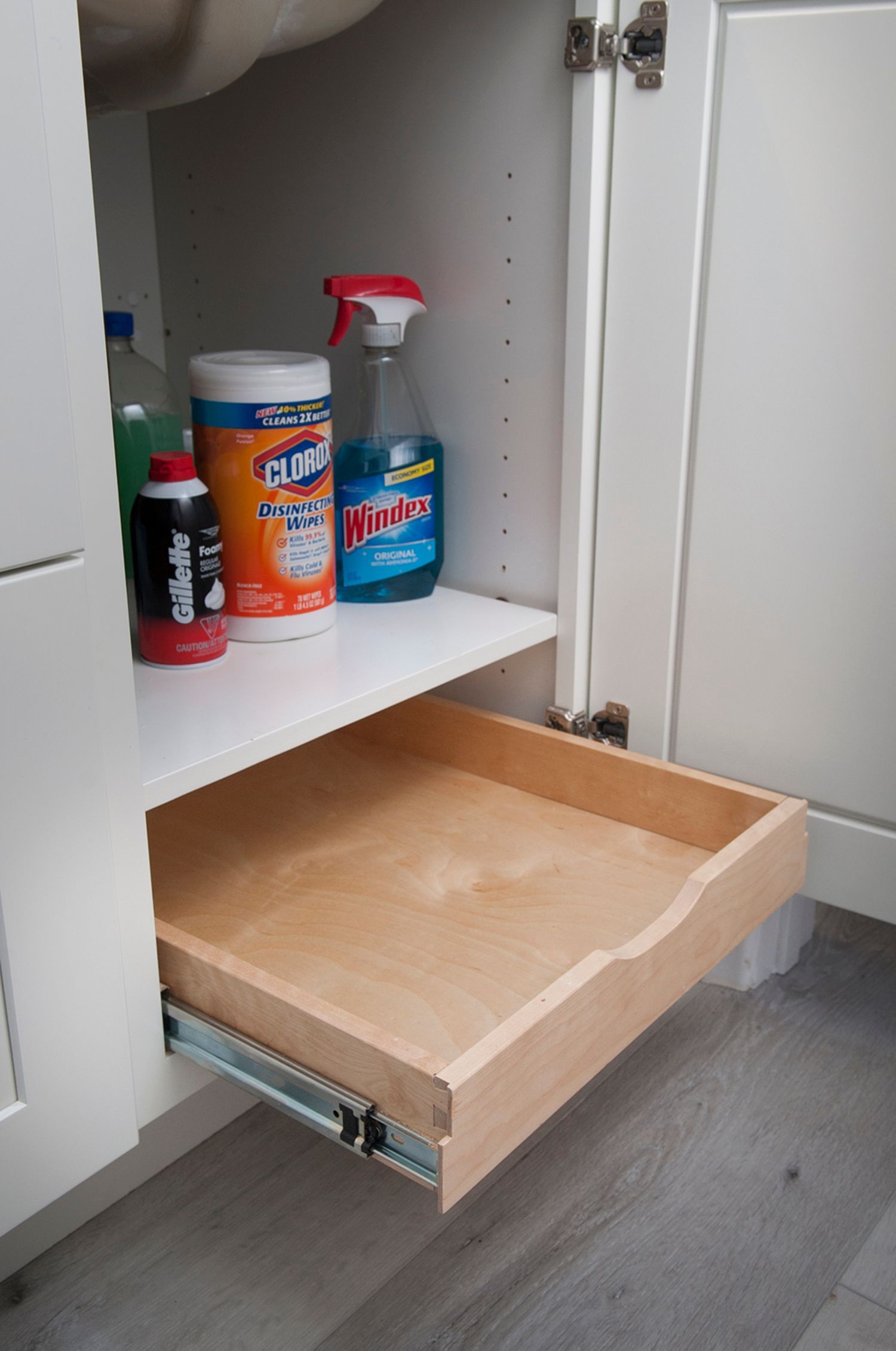 White cabinet under a sink with a pull-out drawer holding cleaning supplies.