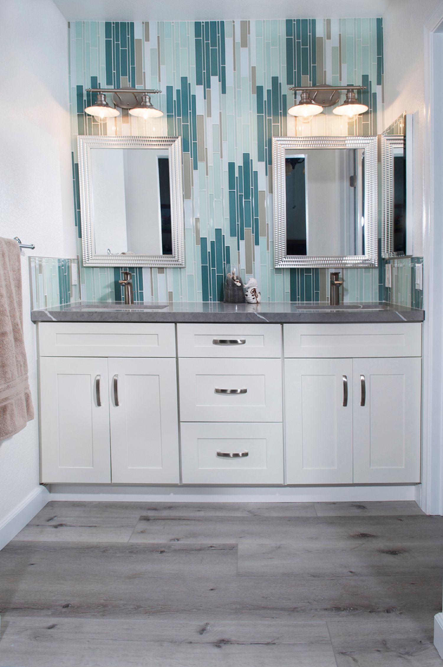 Bathroom with white cabinets, teal backsplash, gray countertop, and two mirrors.