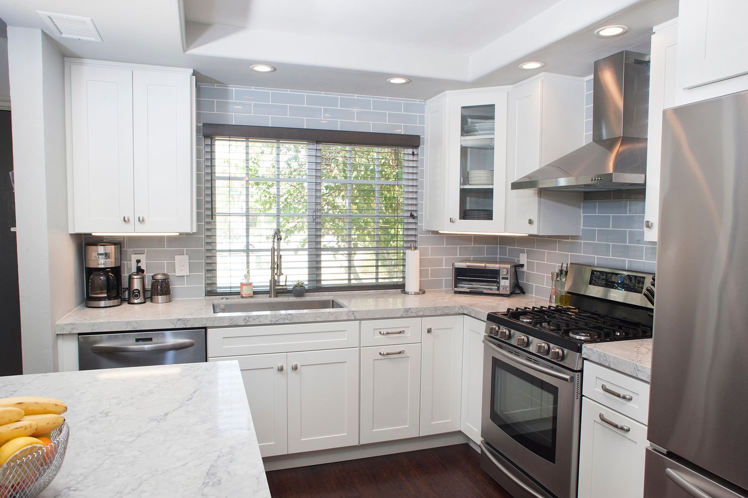 White kitchen with stainless steel appliances, white cabinets, and grey backsplash.