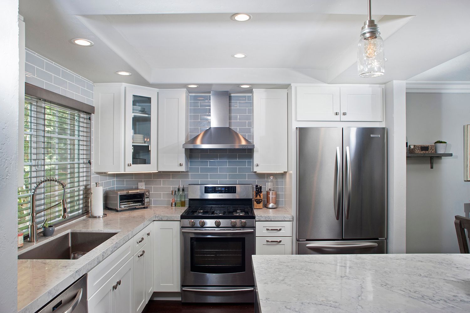 White kitchen with stainless steel appliances, light blue backsplash, and granite countertops.