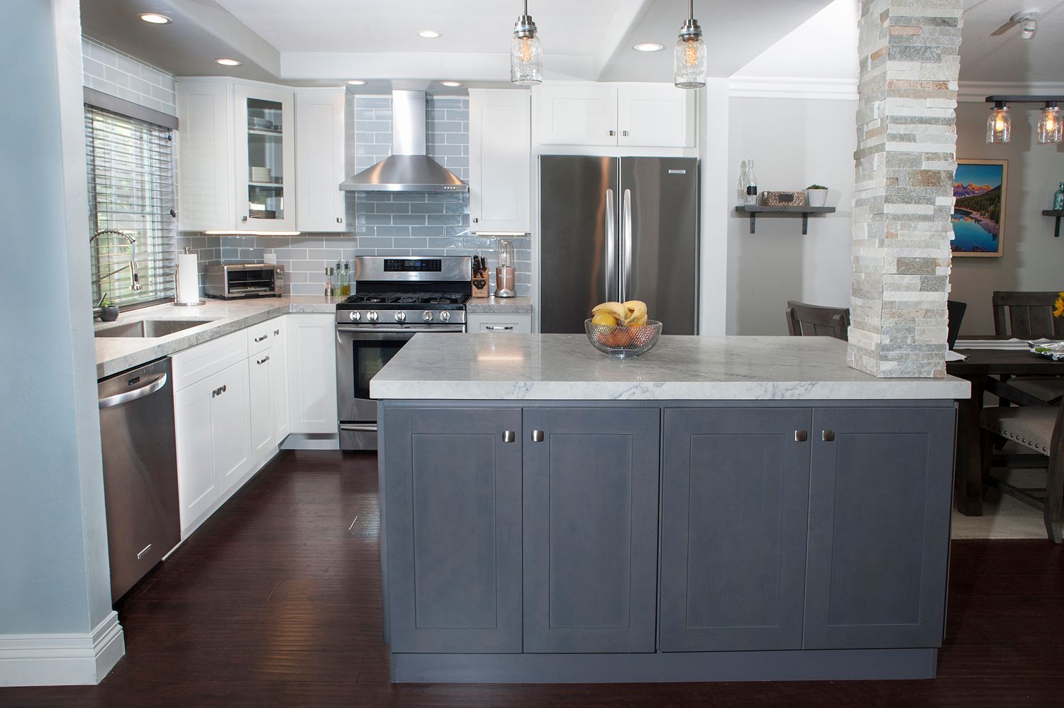 Modern kitchen with white and gray cabinetry, stainless steel appliances, and a stone-covered support column.