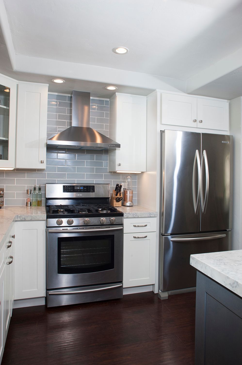 Kitchen with stainless steel appliances, white cabinets, grey backsplash, and dark wood floors.