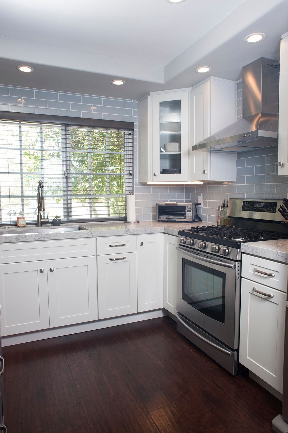 White kitchen with stainless steel appliances, dark wood floor, and grey backsplash.