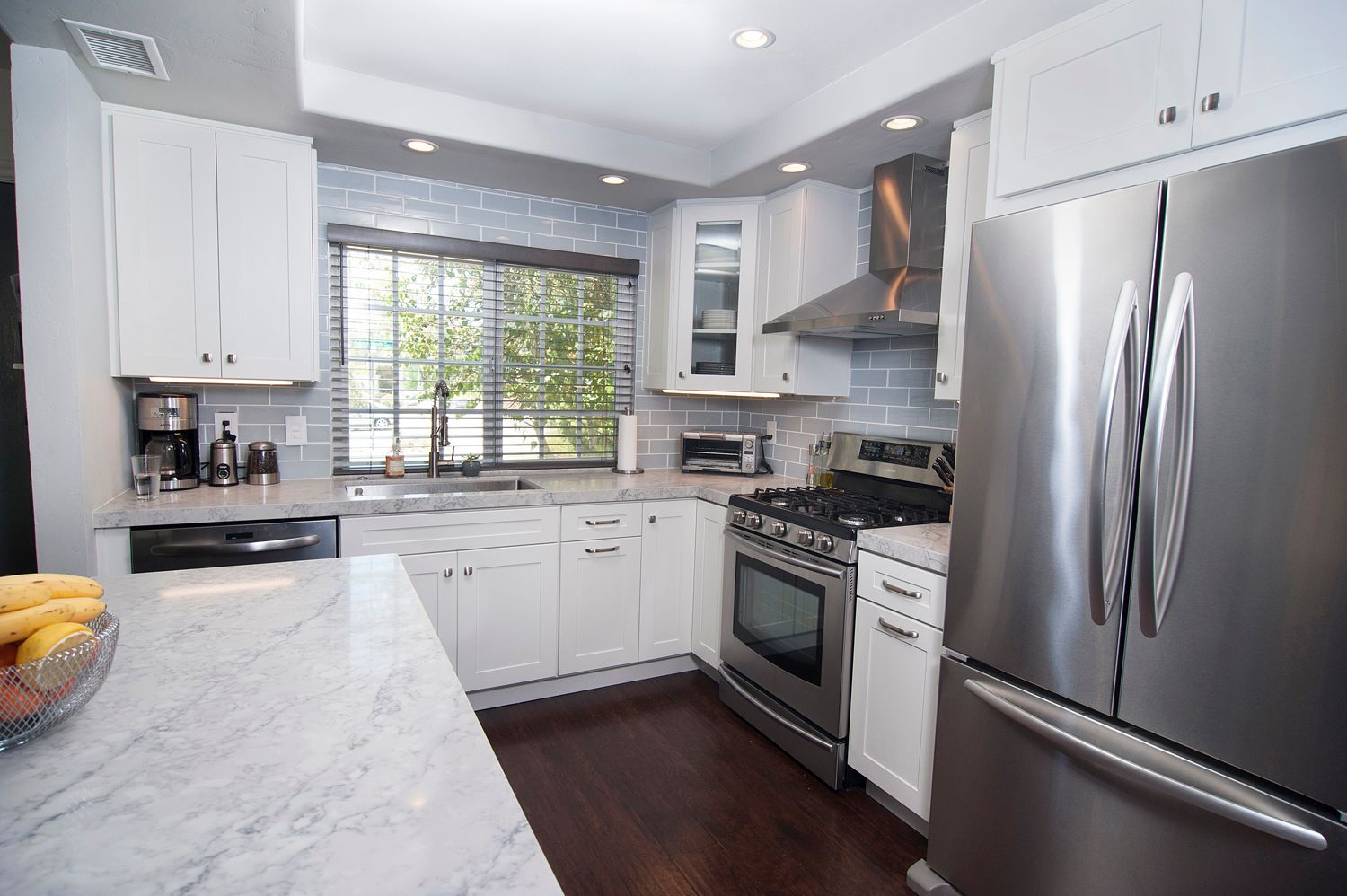 White kitchen with stainless steel appliances, granite countertops, and dark wood floors.