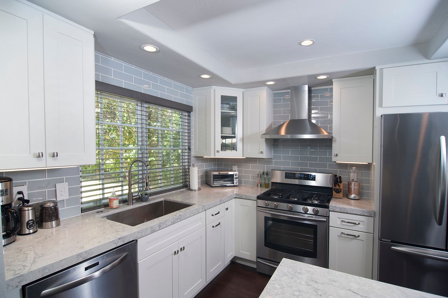 Modern white kitchen with stainless steel appliances and grey backsplash.
